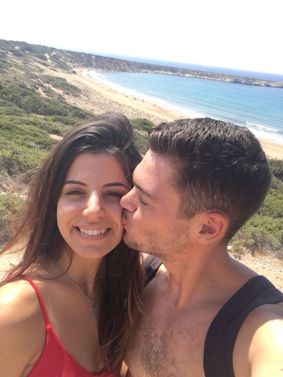 Couple selfie with a kiss on the cheek, beautiful coastal beach below