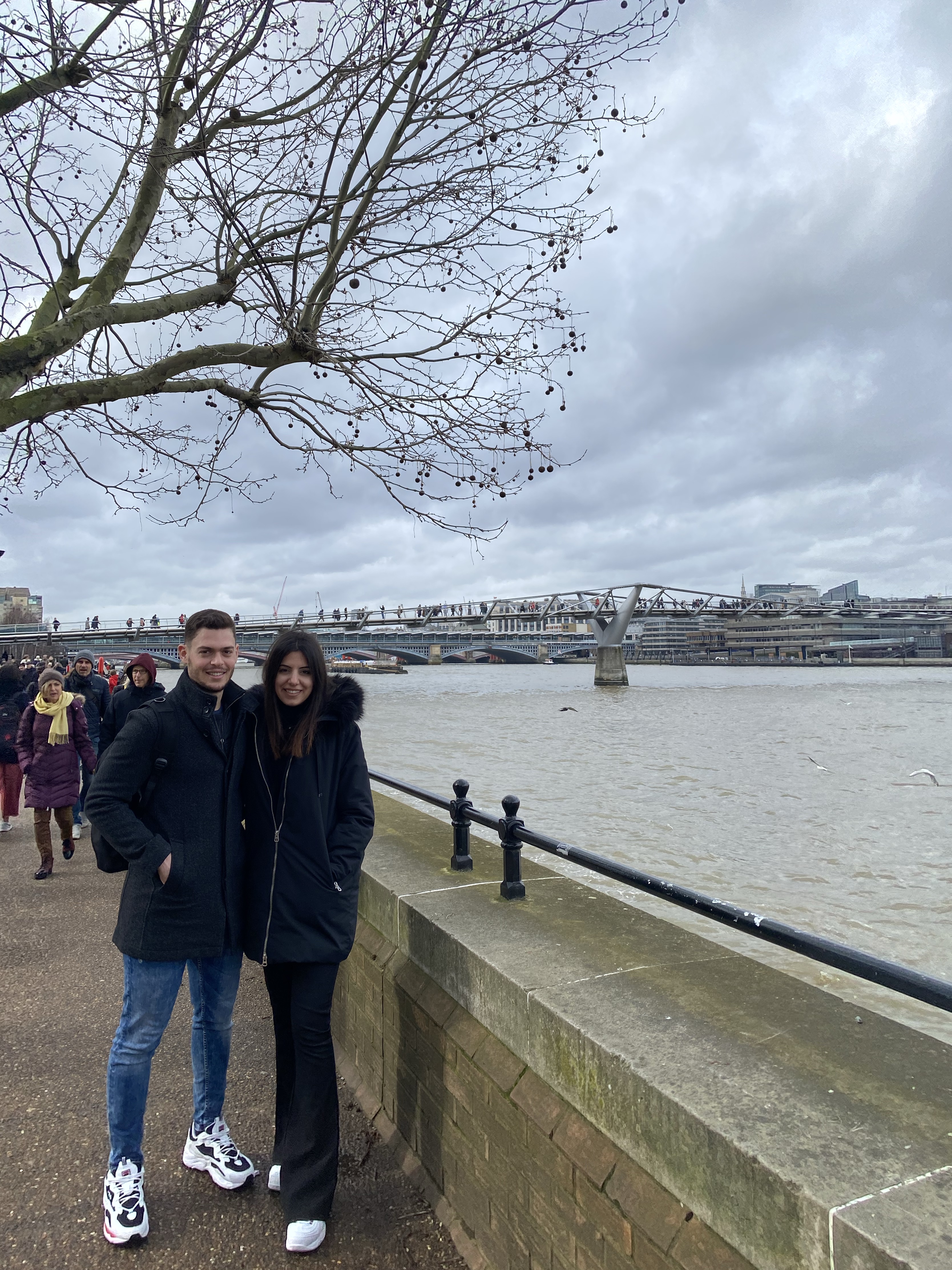 Couple standing together on the Thames embankment in winter coats, Millennium Bridge in the background