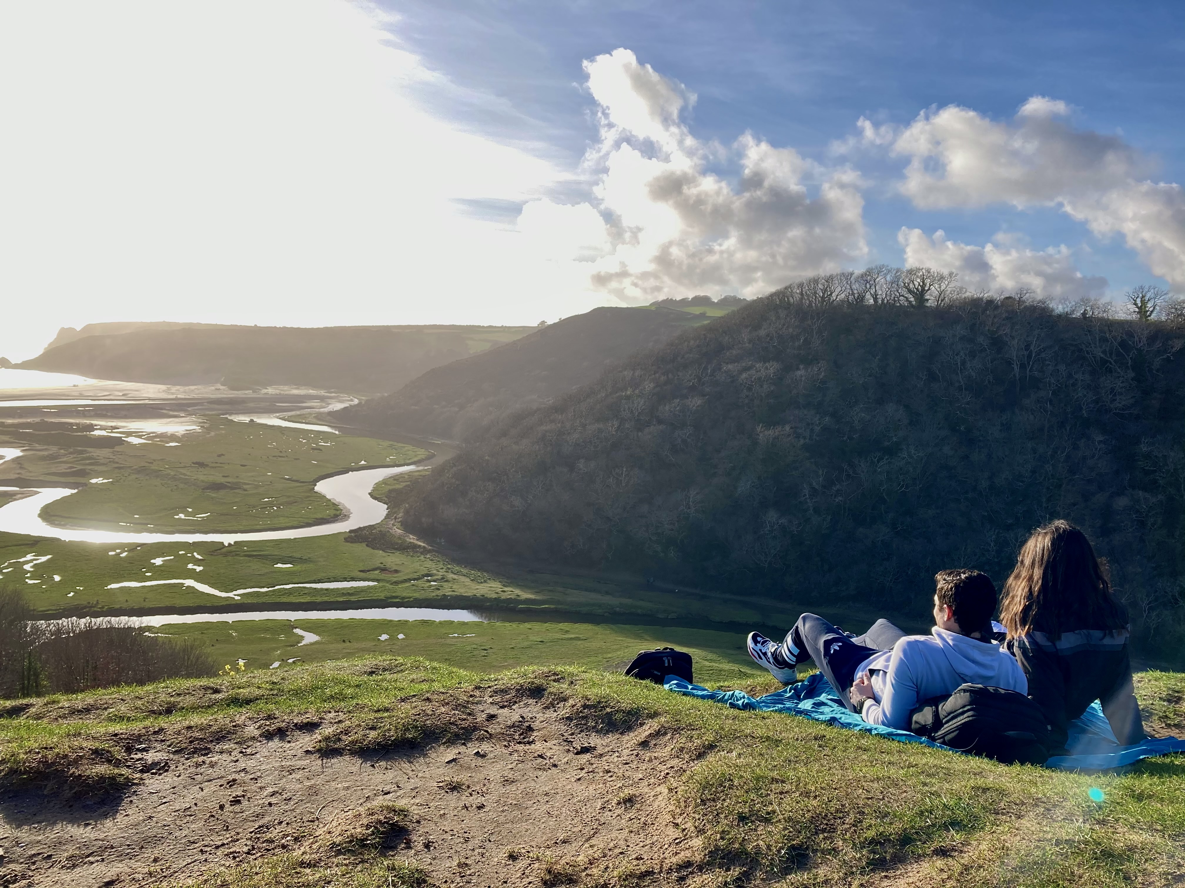 Couple sitting on a sunlit hilltop looking out over a sweeping river valley