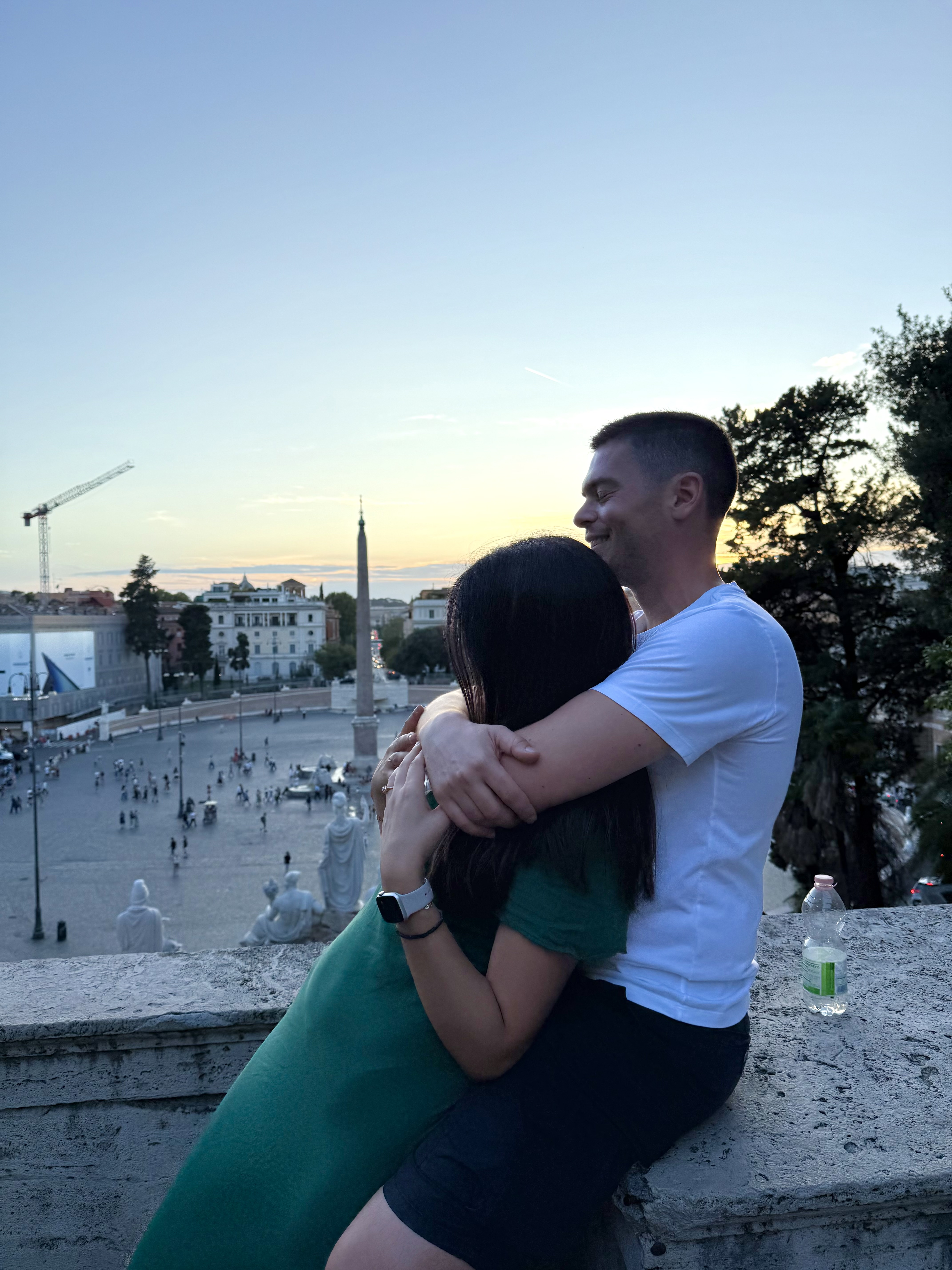 Couple in a close embrace at golden hour above Rome, the Piazza del Popolo spreading behind them